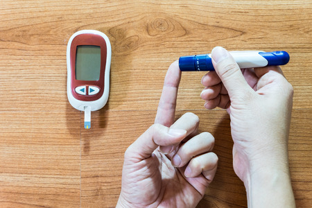 Medicine, diabetes, glycemia, health care and people concept - close up of man hands checking blood sugar level by glucometerの写真素材
