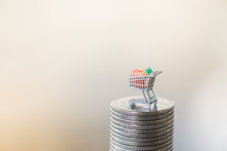 Shopping and e-commerce concept. Close up of miniature shopping cart toy figure on stack of coins with copyspace for textの写真素材