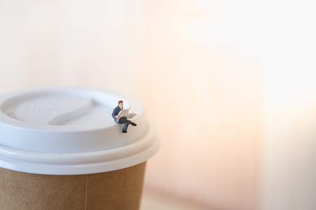 Close up of businessman miniature mini figure sit and read newspaper on the paper cup of take away hot coffeeの写真素材