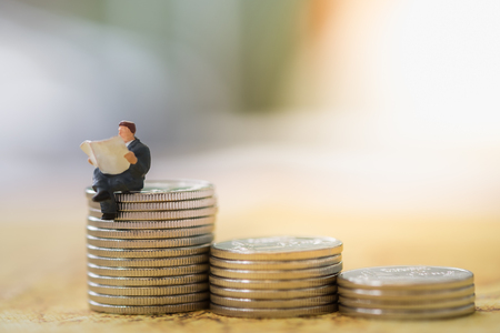 Finance, Business, saving concept. Close up of businessman miniature figure toy sit and read newspaper on stack of coinsの写真素材