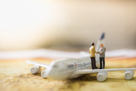 Business and global worldwide concept. Two businessman miniature figures standing, talking, meeting and handshake on wing of airplane model on world map with copy spaceの写真素材