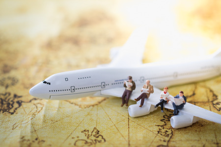 Travel and transportation Concept. Group of miniature figures sitting on wing of airplane on world map and reading a book.の写真素材