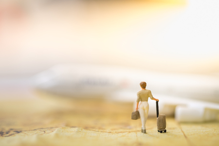 Travel Concept. Business woman miniature figure with luggage walking on world map and airplane toy model in backgroundの写真素材