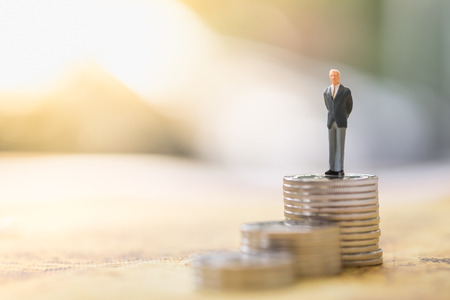 Money and Business Concept. Businessman miniature people figure standing and looking from top of stack of coinsの写真素材