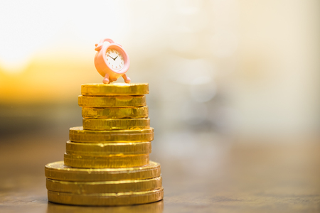 Money and time management concept. Miniature clock on stack of god coins.の写真素材