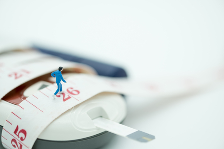 Close up of runner miniature figure running on measure tape binding on Glucose meter with blood sugar test strip and lancet - use for Medicine, diabetes, glycemia, sport, health care and people concept.の写真素材