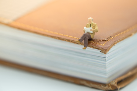 Reading and hobby concept. Miniature mini figures male sitting on a big book and reading a book.の写真素材