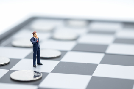 Businessman miniature people figure standing on chessboard with silver coins on black. Business, strategy, planning and work concept.の写真素材
