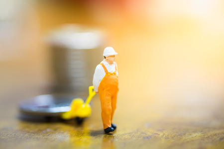 Worker miniature people figure pulling silver coin with stack of coins on wooden table. Money, saving and work concept.の写真素材