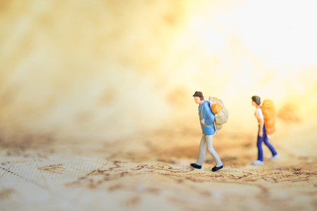 Two traveler miniature people figures with backpack standing and walking on world map. Travel and Journey concept.の写真素材