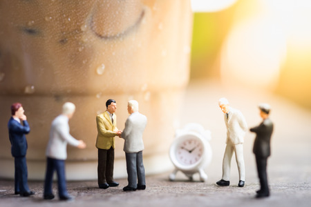 Coffee, Time and Business cooperation concept. Group of businessman miniature people figures meet and hand shake on wooden table close to a plastic cup take away of iced coffee latte with mini clock toy.の写真素材