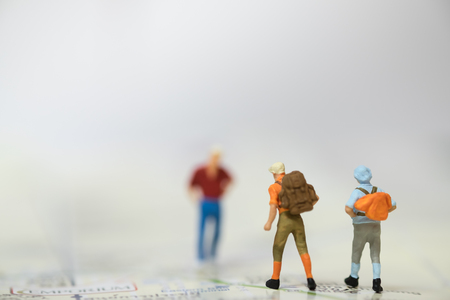 Travelling concepts. Two Traveler miniature people figures with backpack walking on map in front of a man with red shirt.の写真素材