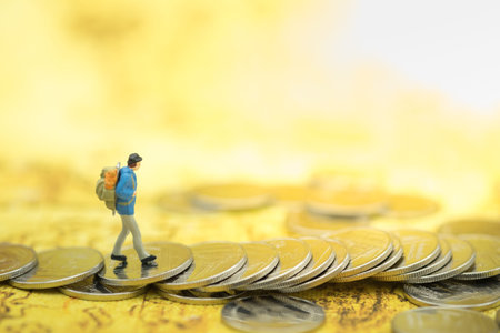 Travel, saving, planing concept. Traveler miniature people figure with backpack walking on coins on...