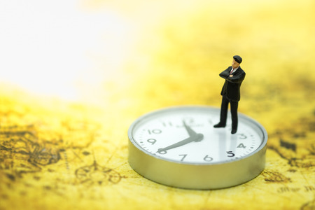Global Business and Time concept. Businessman miniature people figure standing on watch on world map.の写真素材
