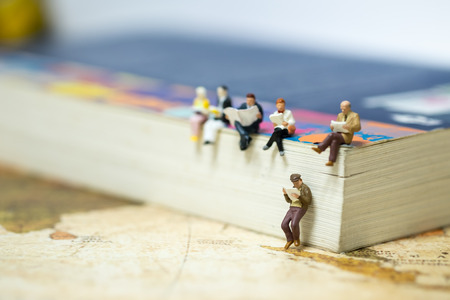 Reading and hobby concept. Group of miniature mini figures businessman, man and woman siting and read a book together on a big book on vintage world map.の写真素材