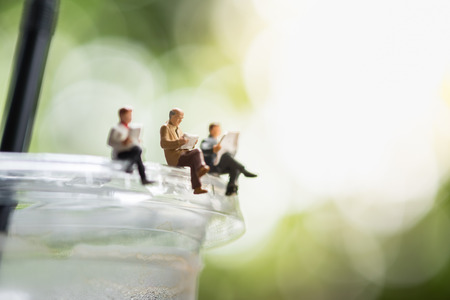 Reading, relaxing, hobby concept. Close up of Group of businessman miniature mini figure sitting and reading a book and newspaper on a take away plastic cup iced coffee.の写真素材