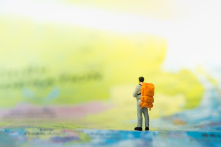 Travel concepts. Traveler miniature mini figures with orange backpack standing and looking to forward on world map.の写真素材