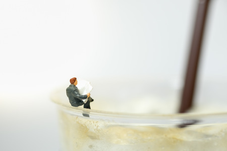 Businessman miniature people figure sitting and reading a newspaper on take away plastic cup of iced coffee.の写真素材