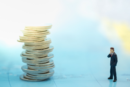 Money, business and Risk concept. Close up of businessman miniature people figure standing and looking to  unsteady stack of silver coins on world map.の写真素材