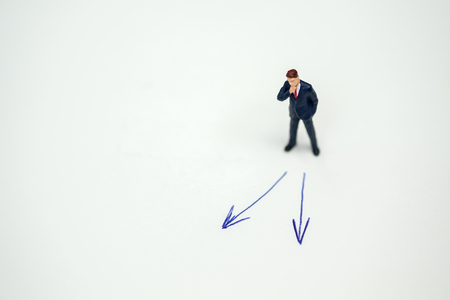 Business direction, decision and planning concept. Businessman miniature figure standing and thinking on paper with 2 arrow sign.の写真素材