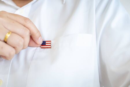 Close up of man hand holding United State of America nation flag pin on white shirt flag.の写真素材
