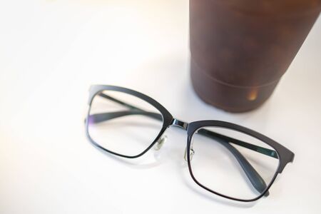 Close up oof readding glasses with plastic cup of iced black coffee on white table.の写真素材