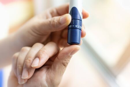 Close up of woman hands using lancet on finger to check blood sugar level by Glucose meter. Use as Medicine, diabetes, glycemia, health care and people concept.の写真素材