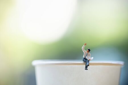 Business concept. Close up of businessman miniature figure sitting and read a newspaper on take away paper cup with copy space.の写真素材