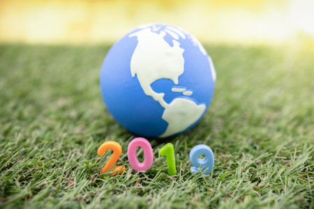 Global new Year 2019 concept. Close up of colorful plastic toy number on grass with mini world ball.