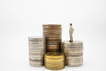 Business, Finance, Saving and secure concept. Close up of businessman miniature figures standing on stack of coins and looking to highest stack on white background and copy space.の写真素材