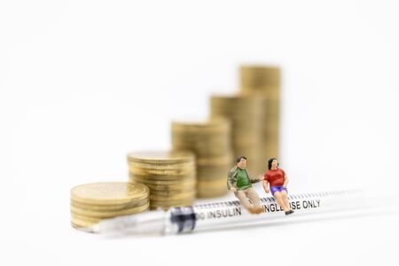 Fat man and woman miniature figure sitting on insulin syringe for control diabetes blood sugar level with stack of gold coins. Use for Medicine,  glycemia, health care, money and people concept.の写真素材