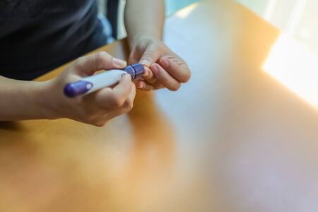 Close up of woman hands using lancet on finger to check blood sugar level by Glucose meter in the morning. Use as Medicine, diabetes, glycemia, health care and people concept.の写真素材