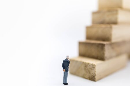 Business, Management and Planning Concept. Close up of businessman miniature figure standing and looking to stack of wooden bloack toy on white background and copyspace.の写真素材