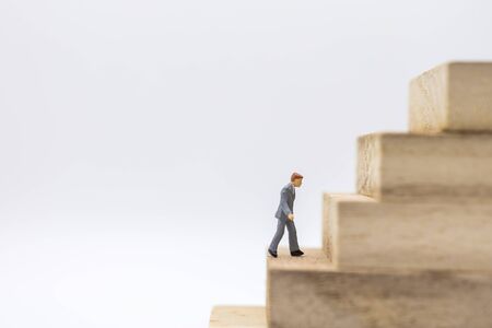 Business, Management Planning and Work concept. Close up of businessman miniature figure walking to top of stack of wooden block toy on white background and copy sapce.の写真素材