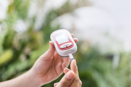 Close up of woman hands using Glucose meter on finger to check blood sugar level. Use as Medicine, diabetes, glycemia, health care and people concept.の写真素材
