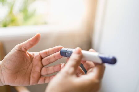 Close up of woman hands using lancet on finger to check blood sugar level by Glucose meter in the morning. Use as Medicine, diabetes, glycemia, health care and people concept.の写真素材