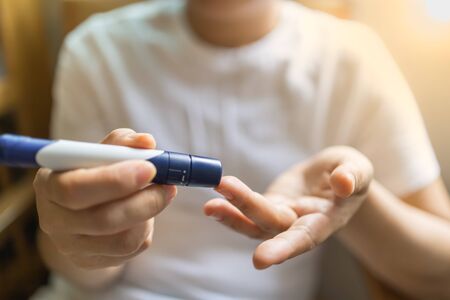 Close up of woman hands using lancet on finger to check blood sugar level by Glucose meter in the morning. Use as Medicine, diabetes, glycemia, health care and people concept.の写真素材