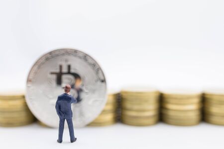 Business, e-commerce, crypto currency, finance and technology concept. Close up of businessman miniature figure standing and looking to bitcoin coin and row of stack of gold coin on white background.の写真素材