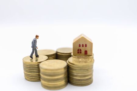 Business, Money, Finance, Home loan and management concept. Close up of businessman miniature figure walking on top of stack of gold coins to mini wooden house toy on white background.の写真素材