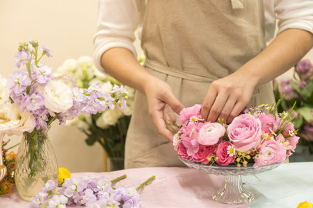 Close up of young woman arranging beautiful pink rose flower bouquet vase on table.