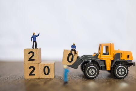 2020 New year , work and Business concept. Close up group of worker miniature people working with toy loader truck machine car loadded number 0 wooden block to stack block on wood table and copy spaceの写真素材