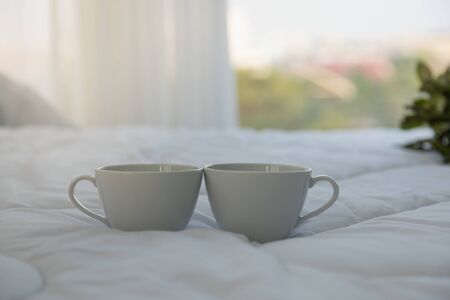 Close up of two white hot cup of coffee on bed in bedroom with copy space in the morning.の写真素材
