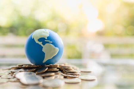 Global Business and Financial, Economic and palnning Concept. Close up of mini world ball on pile of gold coins with green nature background and copy space.の写真素材