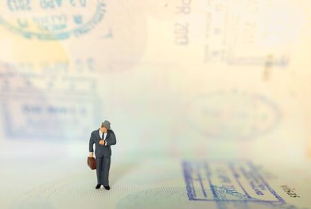 Time, Travel and planning concept. Businessman miniature figure people with suitcase standing and look to wrist watch on passport with immigration stamped and copy space.の写真素材