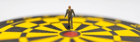 Business Planning, Target and Goal cover Concept. Businessman miniature figure people standing and walking to red center of yellow black dartboardの写真素材