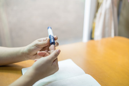 Close up of woman hands using lancet on finger to check blood sugar level by Glucose meter with...