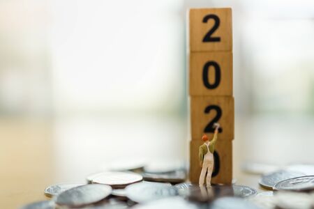 2020 New year, Business, Saving and Planning Concept. Close up of worker miniature figure standing and painting  on stack of wooden number block toy on pile of coins with copy spaceの写真素材