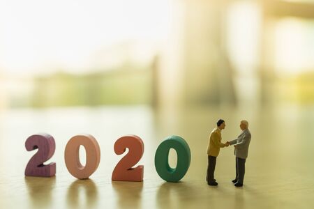 2020 Business  and planning Concept. Two businessman miniature figure people standing and make a hand shake with wooden number and copy space.の写真素材