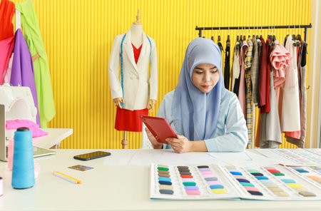 Portrait of beautiful asian muslim woman designer with hijab holding and using computer tablet with ...