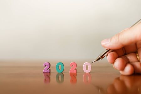 2020 New Year and Planning Concept. Closeup of man hand holding silver pen with colorful wooden number on wood table with copy space.の写真素材